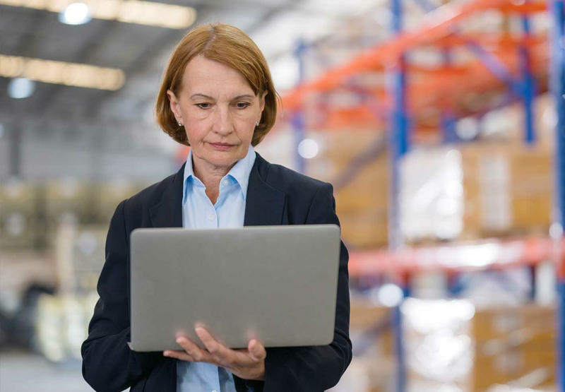 A woman in a suit is looking at a laptop in a warehouse.